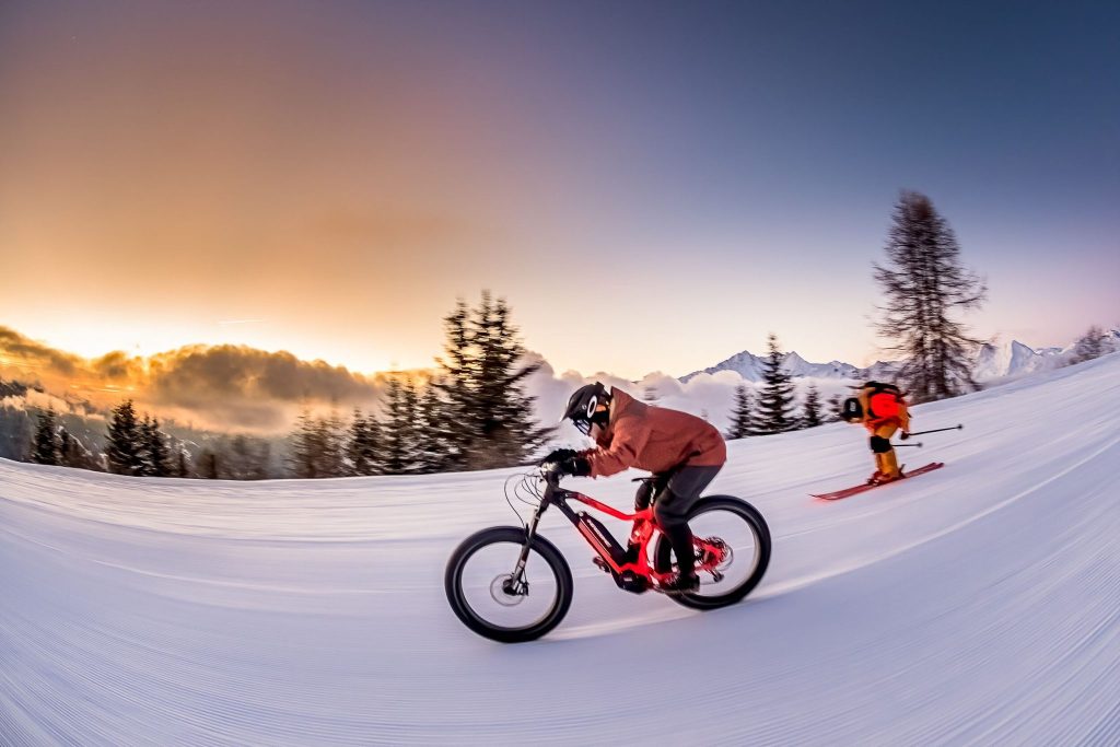 Skier and Biker carving through fresh snow on a mountain slope.